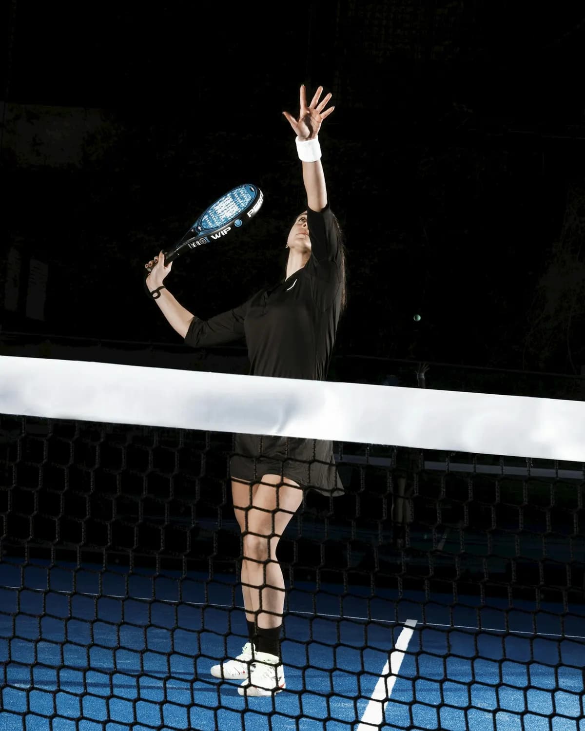 Jogadora de padel a alcançar a bola num court iluminado à noite